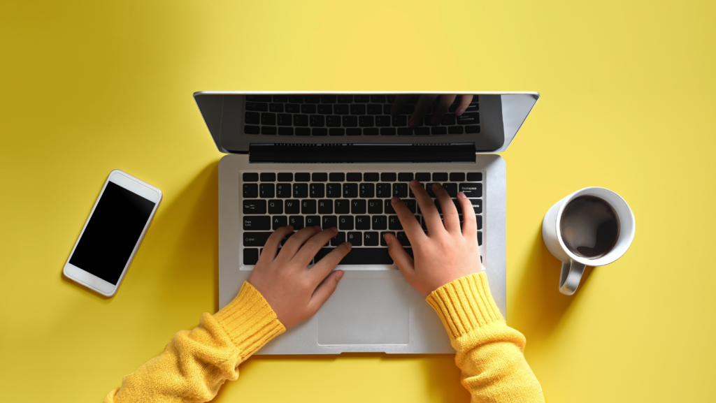 Photo of hands typing on a Macbook with a bright yellow background.